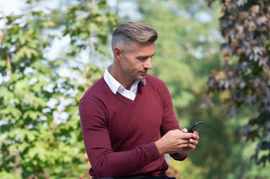 İş adamı dışarıdaki telefonu kullanır. Oturan olgun bir iş adamı. Sonbahar tarzı. Sonbahar parkındaki iş adamı. Kafkasyalı bir adamın günlük bir tarzı vardır. Olgun adam cep telefonu kullanır. Sabit iletişim.