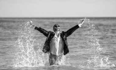 Yaz seyahati. Eğlenceyi keşfet. Kumsalda dinlenen bir iş adamı. Uzaktan kumanda çalışıyor. İş adamı kumsalda iyi eğlenceler. Denizde takım elbiseli mutlu iş adamı. Yaz tatilinde başarılı bir iş adamı.