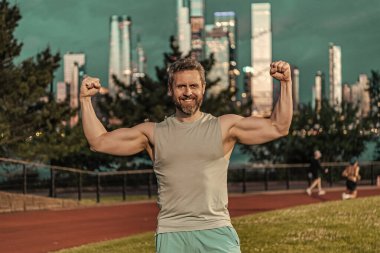 Sporcu pazılarını ve pazılarını göster. Adam pazılarıyla kollarını esnetiyor. Güçlü kaslı sporcu. Dışarıda spor antrenmanı. Antrenmandan sonra sporcu. Spor yapan adam. Pazı kavramı. Vücut geliştirici.