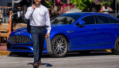 Şirket işi. Takım elbiseli zengin iş adamı. İş portresi. Başarılı bir iş adamı dışarıda evrak çantasıyla dolaşıyor. İş adamı evrak çantasını tutar. Başarılı anlaşmadan sonra işadamı, kırpılmış görünüm.