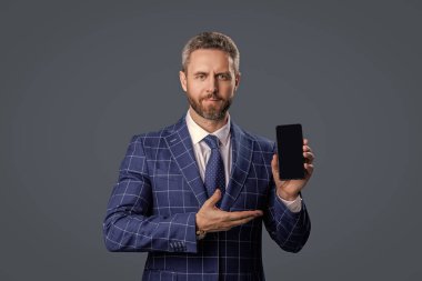 Ürünü sunuyorum. İş uygulamasının reklamı. İspanyol iş adamı telefon ekranını sunuyor. Griler 'de izole edilmiş bir telefon gösteren bir iş adamı. Takım elbiseli adam. Yeni telefon uygulaması.