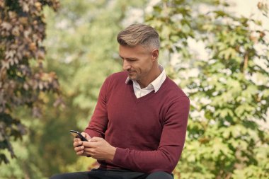 Sonbahar adamı telefonu kullanır. Sıradan bir iş adamı gibi. İş adamı dışarıda telefonla mesajlaşıyor. İş iletişimi tarzı. İnternet işi. İşadamı sonbaharda telefon kullanır. Gülümseyen müdür.