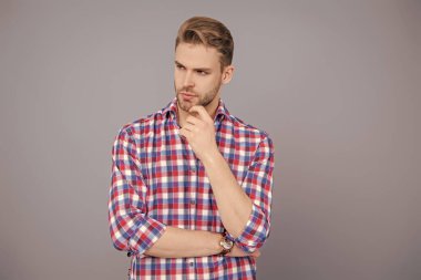 Gündelik giyinen milenyum adamı. Yakışıklı genç adam. Sıradan gömlekli bir adamın portresi. Gri üzerinde kollarını çapraz tutuyor. Tıraşsız erkek derisi. Erkek güzelliği ve saç stili. Erkek saç kesimi.