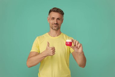 Erkek güzellik kozmetiği. Erkek kozmetik ürünü sunan adam. İzole edilmiş yüz kremi gösteren adam. Olgun adam cilt kremi kullanır. Günlük alışkanlık ve kişisel bakım. Cilt güzelliği. Cilt esnekliğini arttır.