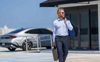 İş adamı evrak çantasını tutar. Başarılı bir anlaşmadan sonra bir iş adamı. Şirket işi. Takım elbiseli zengin iş adamı. İş portresi. Başarılı bir iş adamı evrak çantasıyla dışarıda dolaşıyor, boşluğu kopyala.