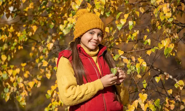 Okuldaki mutlu genç kız, sonbahar yapraklarıyla dışarıda..