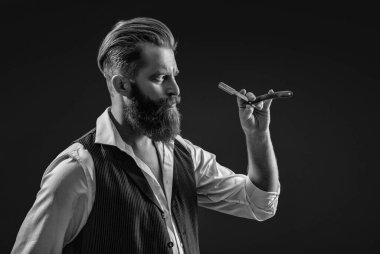 Saç keserken retro bıçak kullanan yakışıklı berber. Modern berber saç kesimi. Siyah sakallı hippi berber. Berberdeki kuaförden sakal kesimi. Moda saç kesimi.