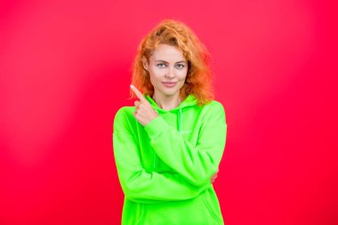 Kızıl saçlı manken kapüşonlu ve kot pantolon giyiyor. Kapüşonlu kadın koşucu. Pembe üzerine izole edilmiş kız kazağı. Kapüşonlu havalı bir kadın. Şık, sıradan tarzda şık bir kız. Reklamlara işaret ediyor..