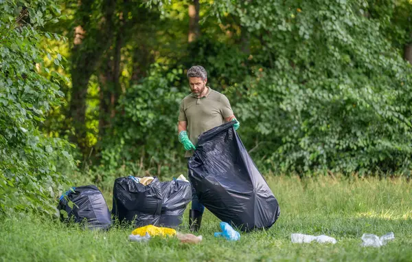 İspanyol ekoloji gönüllüsü lastik eldivenlerle çöp torbalarıyla ormanda, ekolojide çöp topluyor..