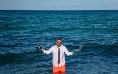Sea Beach 'te serbest çalışan bir adam. İş adamı deniz tatili. Çevrimiçi serbest. Bilgisayarı olan uzaktan kumandalı bir iş adamı. Kumsalda dizüstü bilgisayar kullanan bir iş adamı. Seyahat ve iş. Uzak çalışma ayarları.