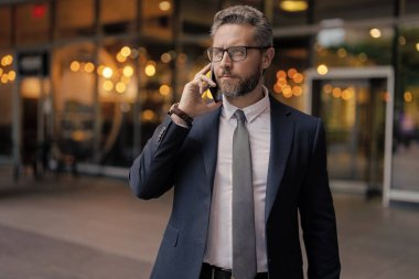 Takım elbiseli adam telefonda konuşuyor. Telefon var. Mobil iletişim. İletişim. İş adamı açık havada akıllı telefondan konuşur. Olgun iş adamı telefon görüşmesi yapar. İş görüşmesi. Boşluk afişini kopyala.
