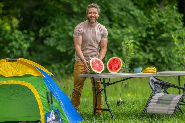 Kamp ve doğa pikniği. Adam kampı. Karpuz kampı pikniği. Lezzetli sağlıklı yiyecekler. Kampta taze yiyecek. Yaz kampında karpuzlu bir adam. Yaz günü doğa yürüyüşçüsü. Mutlu kamp titreşimleri.