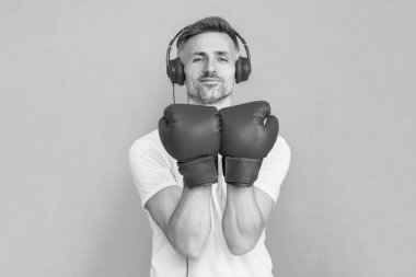 Boks eldivenli sporcu mavi üzerine izole edilmiş. Kulaklık takan olgun bir boksör. Sporcu boks. Güçlü adam müzik dinler. Spor salonundaki sporcu. Spor giyim bölümünde boksör. Egzersiz ve yumruk. Boks eldivenleri.
