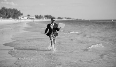 Yaz tatilindeki iş adamı. İnsanoğlunun iş başarısı. Denizde dizüstü bilgisayarla koşan takım elbiseli bir iş adamı. Başarılı bir iş adamı yazın tadını çıkarır. İleri Düşünce.