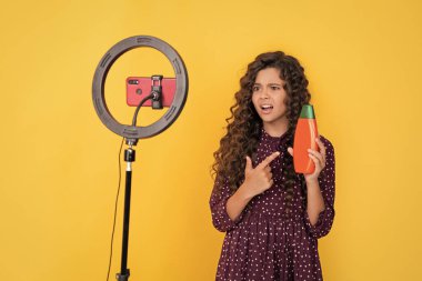 Uzun kıvırcık saçlı çocuk, blog için şampuanı işaret eden video yapıyor..