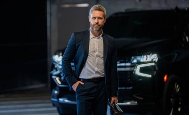 Şirket işi. Takım elbiseli zengin iş adamı. İş portresi. Başarılı bir iş adamı park yerinde evrak çantasıyla duruyor. İş adamı evrak çantasını tutar. Takım elbiseli yakışıklı iş adamı..