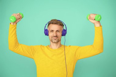 Spor salonu. Atletik egzersiz için müzik. Güçlü sporcu adam seni. Olgun bir adam mavi üzerine izole edilmiş spor eğitimi yapar. Dambılı bir sporcu. Müzikli spor salonu. Fiziksel uygunluk.