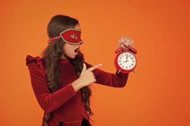 Parti geri sayımı. Parti maskeli, saati olan genç bir kız. Parti sonrası eve geç gelen bir kız. Tatil eğlencesi bitti. Geri sayım. Geç kalan kız turuncudan izole edilmiş. Geç saatte. İşaret parmağı.