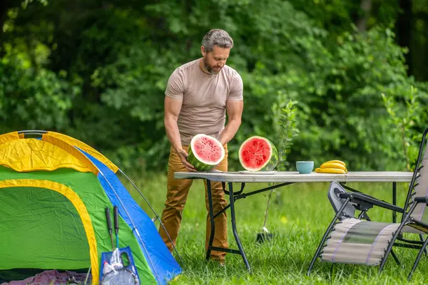 Adam kampı. Karpuz kampı pikniği. Lezzetli sağlıklı yiyecekler. Kampta taze yiyecek. Yaz kampında karpuzlu bir adam. Yaz günü doğa yürüyüşçüsü. Kamp ve doğa pikniği. Kamp yemeği molası.