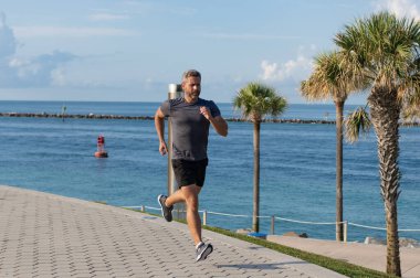 Kumsalda koşan adam. Spor yaşam tarzı. Yazın koşan sporcu. Spor koşuculuğu eğitimi. Sağlıklı yaşam tarzı ve günlük koşular. Koşan koşucu. Spor ve spor. Sabah koşusu.