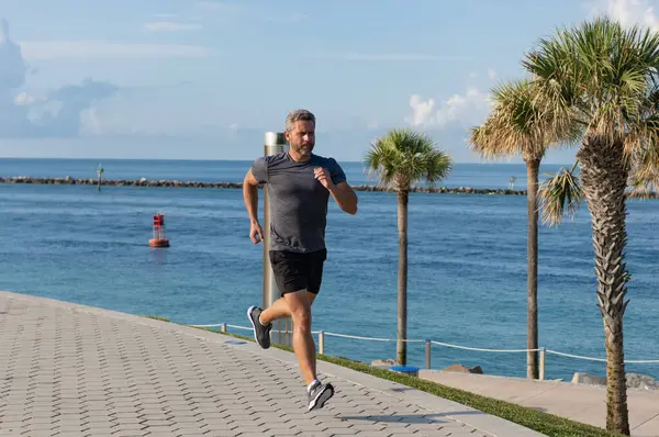 Kumsalda koşan adam. Spor yaşam tarzı. Yazın koşan sporcu. Spor koşuculuğu eğitimi. Sağlıklı yaşam tarzı ve günlük koşular. Koşan koşucu. Spor ve spor. Sabah koşusu.