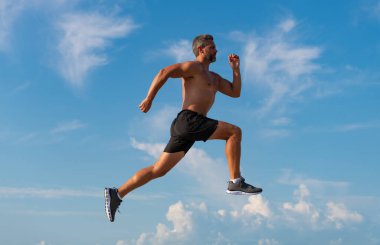 Koşucu çıplak gövde koşuyor. Spor ve sağlık. Mavi gökyüzüne karşı koşan adam. Sağlıklı bir yaşam tarzı. Yazın koşan sporcu. Spor koşucusu egzersiz yapar. Sabah koşusu ile spor yaşam tarzı.