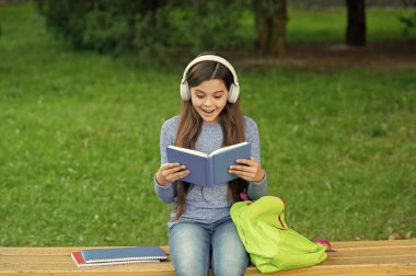 Okula dönelim. Eğitim ve bilgi. Şaşırmış kız sesli kitap dinleyip kitap okuyor. Audiobook kitaba karşı. Öğrenci kız. Okul eğitimi. Liseli kız kitap okur ve dışarıda sesli kitap dinler..