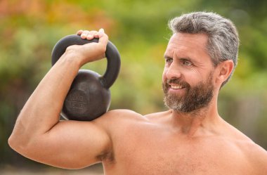 Jimnastik. Sporcu adam kettlebell 'i tutuyor. Ağırlık kaldırma, ağırlık kaldırma antrenmanı. Kettlebell 'le dışarıda egzersiz yapan olgun bir İspanyol. Tencere dibin kara, seninki benden kara. Güçlü adamlar spor yapar..