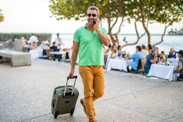 Gezgin telefon kullanıyor. Turist tatili rezervasyonu. Yaz gezisi için seyahat valizi. Yaz gezisini ayarlayan adam. İspanyol turist gezginleri kitabı internette. Seyahat çantalı bir turist. Uçuş rezervasyonu.