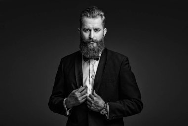 Şık smokin papyonu. Sakallı damat kendinden emin ve hırslı hissediyor. Smokinli erkek giysili adam Griler 'de izole edilmiş. Smokinli adam resmi erkek giyim bölümünde. Yakışıklı sakallı adam smokin giyer. Damat..