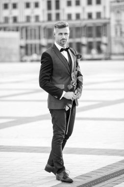 Smokinli zarif bir damat. Damat dışarıda smokin papyon takıyor. Gül ile yakışıklı damat.