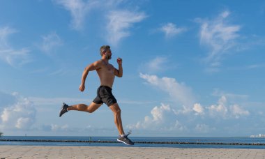 Spor koşucusu egzersiz yapar. Spor yaşam tarzı ve sabah koşusu. Koşucu çıplak gövde koşuyor. Spor ve sağlık. Kumsalda koşan adam. Sağlıklı bir yaşam tarzı. Yazın koşan sporcu, afiş.