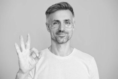 Göz altı kırışıklık önleyici krem sürmüş olgun bir adam. Yüz güzelliği cilt bakımı. Kırışıklık önleyici göz bandı olan adam mavi üzerine izole edilmiş. Yenilenme etkisi. Kozmetoloji. Tamam..