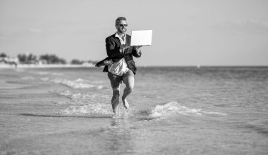 Başarılı bir iş adamı yazın tadını çıkarır. Yaz tatilindeki iş adamı. İnsanoğlunun iş başarısı. Denizde dizüstü bilgisayarla koşan takım elbiseli bir adam. Sıcak yaz işleri..