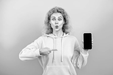 Telefon ekranı sunan bir kadın. Mavide izole edilmiş bir telefon gösteren genç bir kız. Milenyum kadını. Yeni telefon uygulaması. Kız bir ürün sunuyor. Ürünü sunuyorum. İş uygulamasının reklamı.