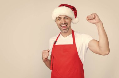 Kırmızı şef önlüğü ve Noel Baba şapkası giymiş olgun bir adam..