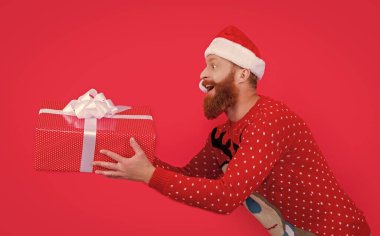 Yılbaşı hediyesiyle şaşırmış bir adam. Mutlu noeller. Noel Baba acele et. Kırmızı ışıkta izole edilmiş noel hediyesini getir..