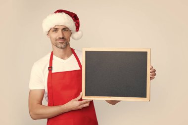Noel Baba şapkalı ve önlüklü neşeli olgun adam fotokopi alanı olan karatahtayı tut..