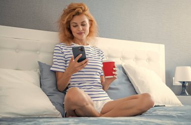 Telefonda internette kahve sörfü yapan neşeli bir kadın. Evde telefonuyla internette sörf yapan bir kadın. Kadının evinde internet sörfü.