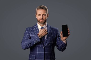 İspanyol iş adamı telefon ekranını sunuyor. Griler 'de izole edilmiş bir telefon gösteren bir iş adamı. Takım elbiseli adam. Yeni telefon uygulaması. Ürünü sunuyorum. İş uygulamasının reklamı. İnternette çalış.