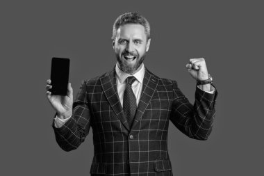 Takım elbiseli adam. Yeni telefon uygulaması. Ürünü sunuyorum. İş uygulamasının reklamı. İspanyol iş adamı telefon ekranını sunuyor. Griler 'de izole edilmiş bir telefon gösteren bir iş adamı. Başarı için mutluyum..