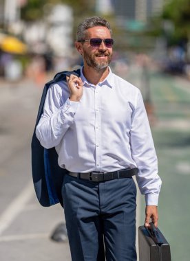 Takım elbiseli zengin iş adamı. İş portresi. Başarılı bir iş adamı dışarıda evrak çantasıyla dolaşıyor. İş adamı evrak çantasını tutar. Başarılı bir anlaşmadan sonra bir iş adamı. Şirket işi. Liderlik.