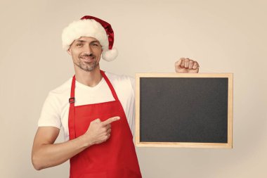 Noel Baba şapkalı ve önlüklü mutlu olgun bir adam tahtada fotokopi uzayı ile işaret ediyor..