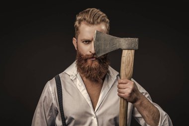 Siyaha izole edilmiş baltalı askılı vahşi bir adam. Saçları kızıl saçlı, olgun bir adam. Acımasız erkek modası. Erkek vahşeti. Antika pantolon askılı, eski tip bir gaddar adam. Berber konsepti.