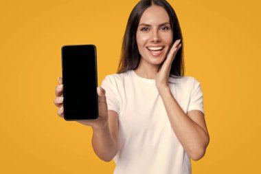 Kız reklam veriyor. Ürünü sunuyorum. İş uygulamasının reklamı. Telefon ekranı sunan bir kadın. Sarıda izole edilmiş bir telefon gösteren genç kız. Milenyum kadını. Yeni telefon uygulaması. En iyi teklif.