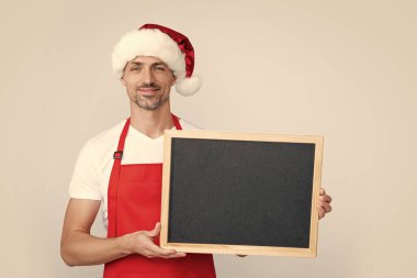 Noel Baba şapkalı ve önlüklü olgun bir adam elinde fotokopi alanı olan bir tahta tutuyor..