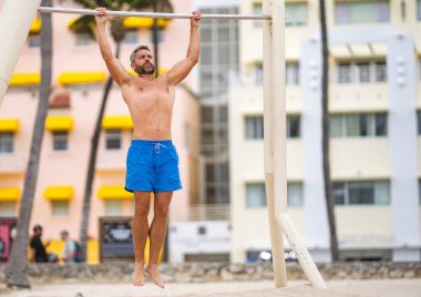 Adam yanaşıyor. Güçlü gövde kası olan kaslı bir sporcu. Spor barfiks egzersizi. Spor eğitimi. Sporcu adam egzersiz yapıyor. Erkek kaslı sporcu açık hava spor salonuna yanaşıyor..