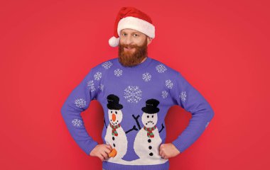 Kırmızı arka planda izole edilmiş Noel Baba şapkası ve süveteri olan beyaz, neşeli bir adam. Adam Noel 'i kutluyor. Mutlu Noeller..