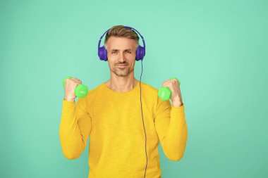 Olgun bir adam mavi üzerine izole edilmiş spor eğitimi yapar. Dambılı bir sporcu. Müzikli spor salonu. Spor salonu. Atletik egzersiz için müzik. Güçlü sporcu adam seni. Sportmenlik.