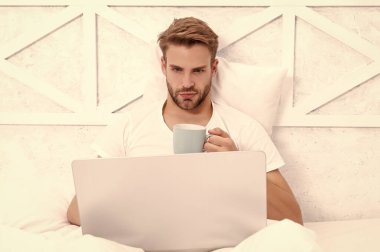 Adam yatakta yatıp dizüstü bilgisayarla internette sörf yapıyor. Bilgisayarda evden çalış. Hafta sonu işkolik. Sabah kahvesi hazır. Yatakta serbest çalışan. Milenyum adamı evde dizüstü bilgisayarda çalışıyor..